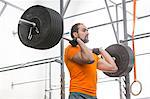 Confident man looking away while lifting barbell in crossfit gym