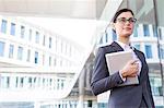 Confident businesswoman holding tablet PC outside office building