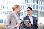 Happy businesswomen with tablet PC and disposable cup conversing outside office building