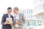 Happy businesswomen using digital tablet outside office building