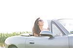 Happy woman holding map while sitting in convertible against clear sky