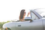 Woman reading map in convertible against clear sky on sunny day