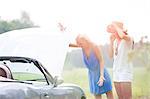 Worried female friends examining broken down car on sunny day