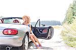 Thoughtful woman sitting in convertible on country road against clear sky