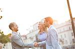 Happy businessmen shaking hands in city against clear sky