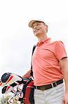 Happy middle-aged man looking away while carrying golf bag against clear sky