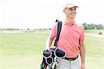 Happy middle-aged man looking away while carrying golf bag