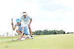 Man with woman aiming ball on golf course against sky