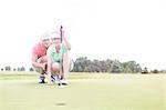 Man assisting woman aiming ball on golf course against clear sky