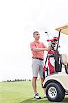 Middle-aged man standing by cart at golf course