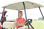 Middle-aged man driving cart at golf course