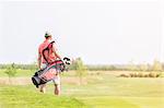 Rear view of man carrying golf club bag while walking at course