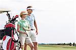 Smiling man and woman standing at golf course against clear sky