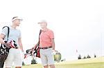 Smiling men talking at golf course against clear sky