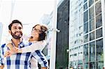 Happy man giving piggyback ride to woman in city