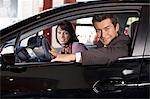 Portrait of young couple sitting in a new car at showroom