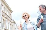 Smiling middle-aged couple holding ice cream cones on sunny day