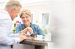 Happy middle-aged couple using mobile phone at sidewalk cafe