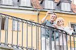 Happy middle-aged couple taking selfie through digital camera against building