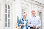 Happy middle-aged couple standing with arm in arm outside building