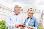 Middle-aged couple reading guidebook outside building