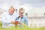 Smiling middle-aged couple reading guidebook outdoors