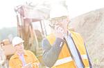 Happy engineer using walkie-talkie on construction site with colleague in background