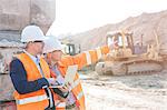 Supervisor showing something to coworker holding laptop at construction site