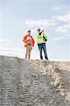 Low angle view of architect showing something to colleague at construction site against sky