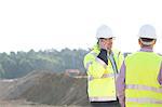 Supervisor using mobile phone while standing with colleague at construction site against clear sky