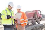 Engineers using laptop at construction site against clear sky on sunny day