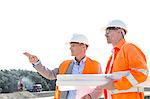 Male engineers discussing at construction site against clear sky