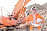 Confident architect holding hardhat and blueprints at construction site