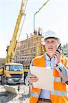 Male supervisor using walkie-talkie while holding clipboard at construction site