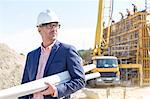 Confident architect holding rolled up blueprints at construction site