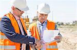 Engineers examining documents on clipboard at construction site against clear sky