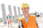 Happy architect looking away while holding clipboard at construction site