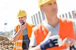 Middle-aged male worker using walkie-talkie with colleague in foreground at construction site