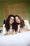 2 teens playing with their mobile phone on a bed