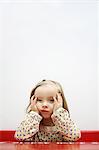 A 3 years old girl sulking, head in hands, leaning on a school desk