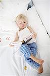 Little boy lying down on his bed reads a book