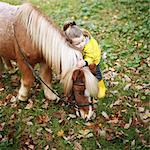 A little girl kissing a pony while he is grazing