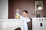 A little boy taking some cookies in a jar