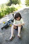 A 5 years old girl near her bike, after falling on a country road