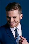 man in blue suit, tie, beard; blue background,