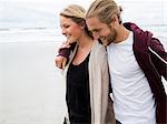 Young man and young woman walking on a beach, smiling.