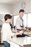 Couple looking at smartphone together while preparing food in kitchen