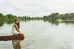 Girl sitting on dock with feet dangling in lake, portrait