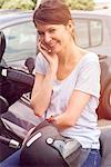 Woman sitting on parked motorcycle, talking on cell phone