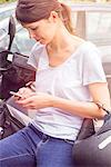 Woman leaning against motorcycle, text messaging with cell phone